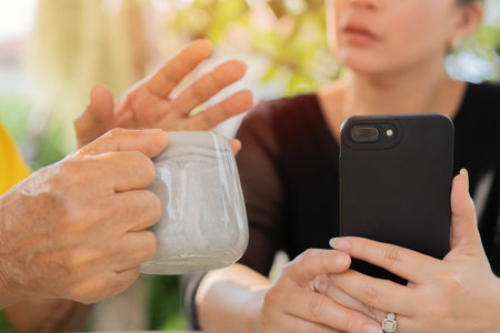 Close-up shot of an Asian woman using her smartphone while talk with her grandfather in the garden....