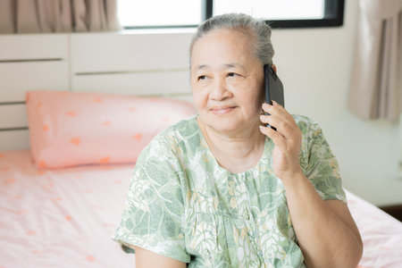 Close up portrait of an old Asian woman happily using her smart phone with her family in bedroom at morning.の写真素材