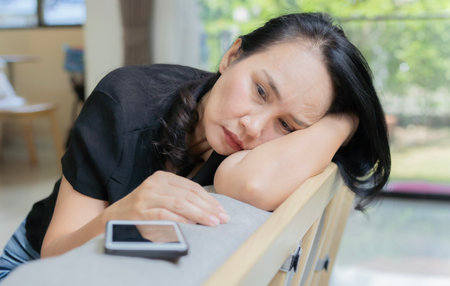 Jealous woman sitting on sofa looking phone feeling sad waiting for call, frustrated woman upset or worried receiving bad news in mobile message on smartphone at home. Selective focus.の写真素材