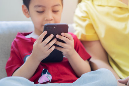 Little boy sitting with mom and watching cartoons on smartphone together. Selective focus, family...