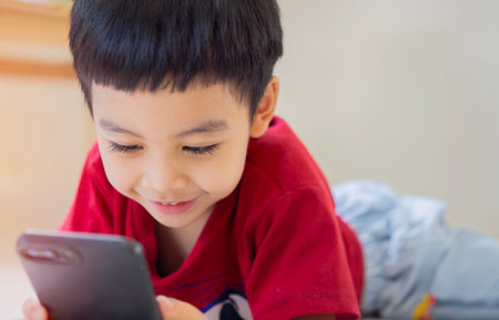 Fun on your smartphone. The Happy Asian little boy is playing the application on the smartphone while lying on the floor at home.の写真素材