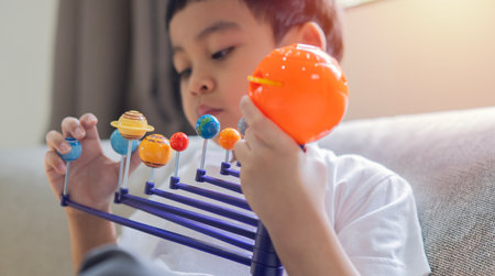 Shot of little child boy sit at sofa and playing planet model toy. Creative educational game. Selective focus, copy space.の写真素材