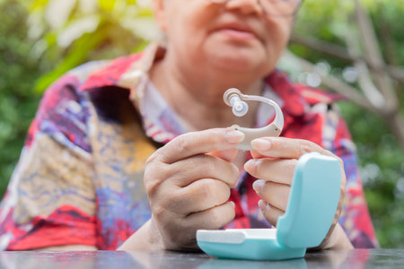 Active senior woman holding hearing aid in hand over nature background. Selective focus. Hearing Aid Concept.の写真素材