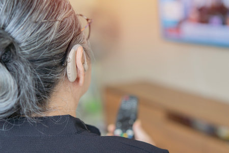Close-up of mature woman wearing hearing aid and watching TV at home. Selective focus, copy space. Deafness device concept.の写真素材