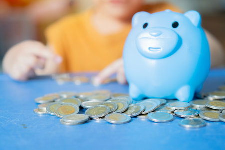 Kid putting coin into pink piggy bank. Happy boy saving money, cash for purchase learning economy, investment, planning future counting budget.の写真素材