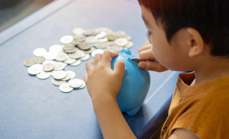 The child manages and deposits his finance, Investment concept. Back view of Asian litte boy holding blue piggy bank and putting the coins.の写真素材