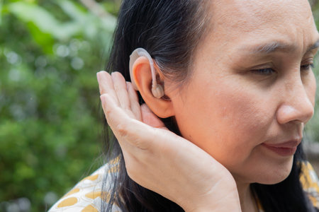 Side view of attractive Asian adult woman with hearing aid over nature background. Healthcare and...