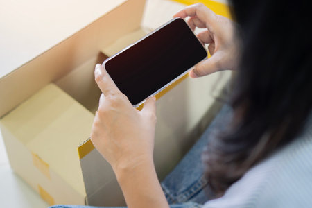 Back view of female holding phone mock up screen and take photo of commercial shipping box delivery order on smartphone. Copy space.の写真素材