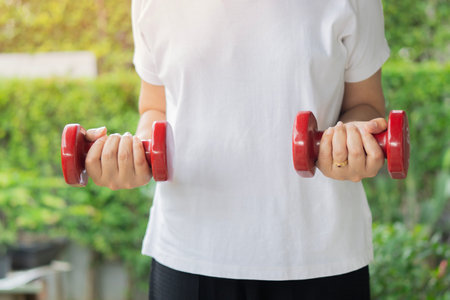 Cropped image of mature females with red dumbbells and working out in the open air. Retirement workout concept.の写真素材