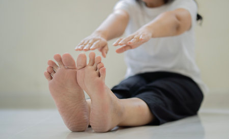 Cropped shot of middle-aged woman in a white  t-shirt is doing exercises while sitting on the floor at home. Retirement sports and health concept.の写真素材