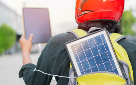 Back view of man with portable solar panel in backpack and tablet while sitting on motorcycle. Integration of sustainable renewable energy into everyday life concept.の写真素材
