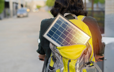 Close-up of yellow and gray backpack on mans back portable solar panel on city road background. Concept of sustainable lifestyle and renewable energy.の写真素材