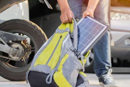 Cropped view of handsome man putting portable solar panel into backpack in the home garage before leaving. Sustainable lifestyle and renewable energy concept.の写真素材