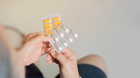 Back view close-up of mature middle-aged woman sitting at home holding pills with copy space.. Care for the health of old people concept.の写真素材