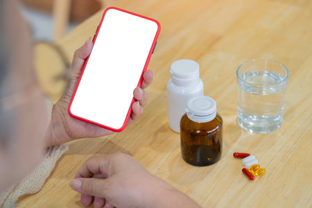 Mature woman with phone isolate screen and medicine bottle with glass of water on the wooden table. Copy space.の写真素材