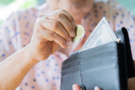 Asian senior woman holding coins and banknotes money in black wallet. Poverty, saving problem in...