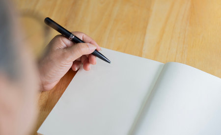 Rear view of senior woman planning idea on notebook using a pen to write in diary on the wooden table. Copy space.の写真素材