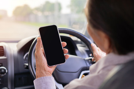 Rear view shot of middle aged Asian man driving car and using smartphone with blank screen....