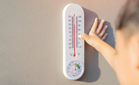 The boy learn to checking the numbers on a thermometer on a gray wall outside the house with copy space. Temperature checking concept.の写真素材