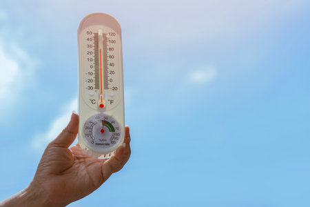 Human hand holding thermometer with a sky background. Concept of global warming. Close up, vertical...