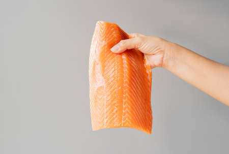 Side view of a piece of salmon in hand on light gray color background with copy space. Cooking inspiration concept.の写真素材