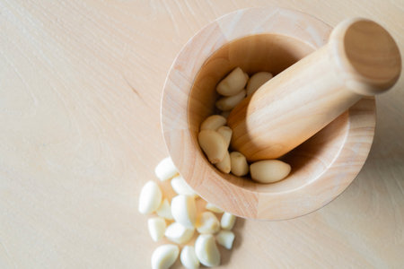 Top view of wooden mortar and pestle with fresh pieces of garlic inside over wooden background with copy space.の写真素材