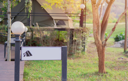 Empty blank sign on a steel pole with copy space for text in front of a tent area in a rural resort at background.の写真素材