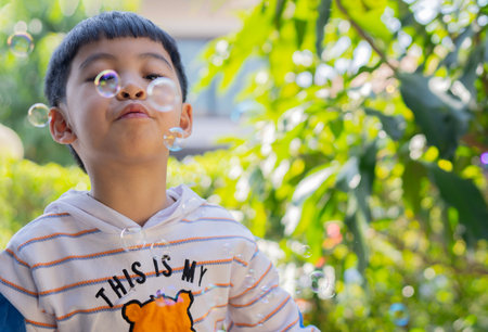 Cute little Asian boy blowing bubbles at outdoor on a summer day. Copy space, selective focus.の写真素材