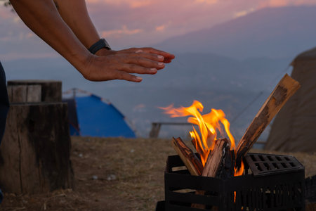 Side view of man warming his hands up on camp fire in winter on the high mountain.
