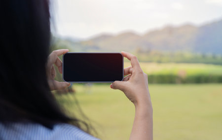 Back view of woman holding phone over scenery background. Accessibility of mobile communications and...