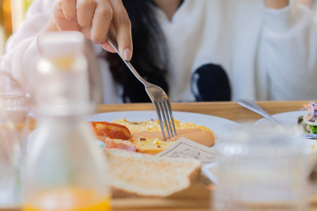 A fork in hand. Breakfast on the table. American style breakfast with fried eggs, sausage and toast. Selective focus.の写真素材