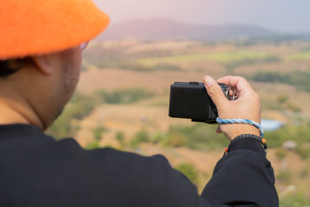 Back view of tourist with orange hat taking photos with camera at mountain landscape. Selective focus.の写真素材