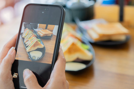 Close-up female hands using smart phone taking photo of sandwiches and coffee on wooden table....