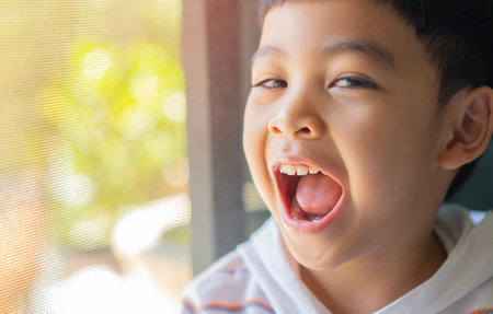 Close-up happy little Asian boy in white tshirt laughing at camera in the livingroom at home.の写真素材