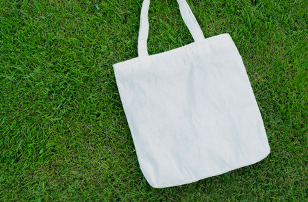 Eco friendly concept with white canvas tote bag on the green lawn background. Eco blank shopping sack with free copy space,の写真素材