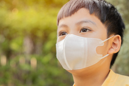 Close-up side view portrait of little Asian boy wearing medical face mask at home with nature background. Copy space.の写真素材