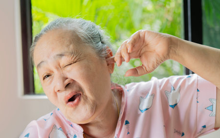 Deaf. Portrait senior Asian woman with ear pain covering ears with fingers hand in the livingroom at...