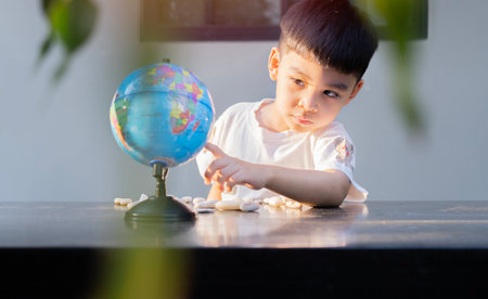 A young child boy is looking and pointing a planet earth model while sitting at outdoor. Kids...
