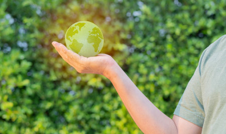 Side view of man holds a green planet Earth on a background of real nature. Symbol of sustainable development and renewable energyの写真素材