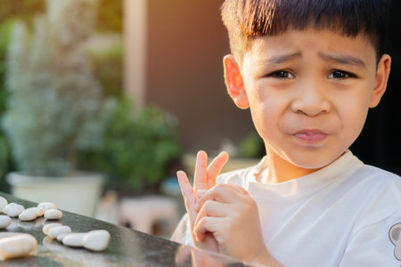 Little Asain child boy sitting outside in the garden at home suffering pain on hands and fingers, arthritis inflammation. Kids Healthy concept.の写真素材