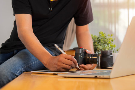 Cropped shot of young cheerful photographer man use photocamera while working in his office.の写真素材