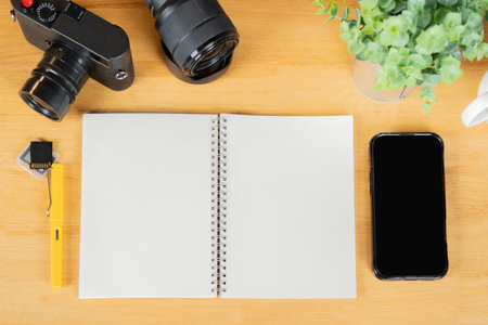 Flat lay of blank paper notebook with camera, memory cards, lens and phone on wooden table background. Copy space.の写真素材
