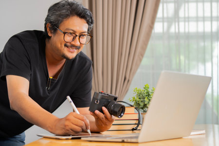 Happy adult freelance handsome photographer at home, working on laptop in home office. Selective...