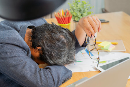 Lazy adult man sleeping in work time, male officer feeling tired and dizziness, he holding a eyeglasses while rest face on work table, overwork and hardwork problem.の写真素材