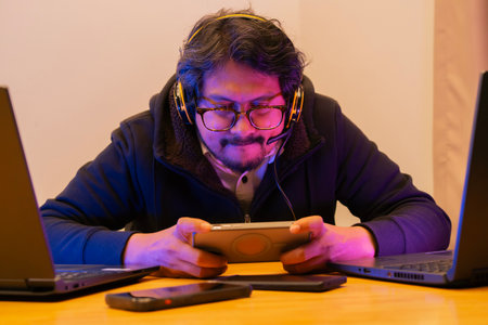 Adult blogger man with glasses holding a mobile phone and play an online game while relaxing in a studio. Selective focus.の写真素材