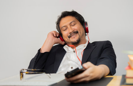Relaxed male professional with eyes closed enjoying music during a break from work at the office. Selective focus.の写真素材