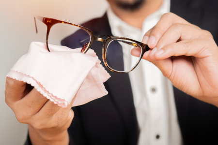 Close-up man is cleaning his eyeglasses with a fabric cloth, dirt and protection with fabric tissue. Reading and lens eye car concept.の写真素材