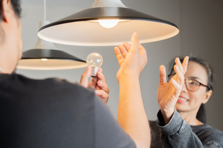 Happy young family couple changing a light bulb together. Cheerful, smiling woman and man standing...