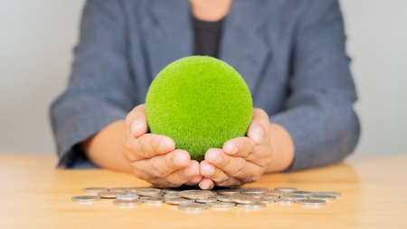 Cropped image of businessman holding a green earth globe with pile of coins on the wooden table. Investment conceptの写真素材