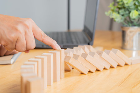 Risk concept with hand of businessman stopping and protection the domino effect on wooden table. Selective focus.の写真素材